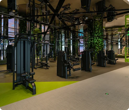 Moderne fitnessruimte met meerdere zwarte fitnessapparaten, spiegelwanden en groene accenten. De ruimte voelt strak en hightech aan en stimuleert energie en focus.